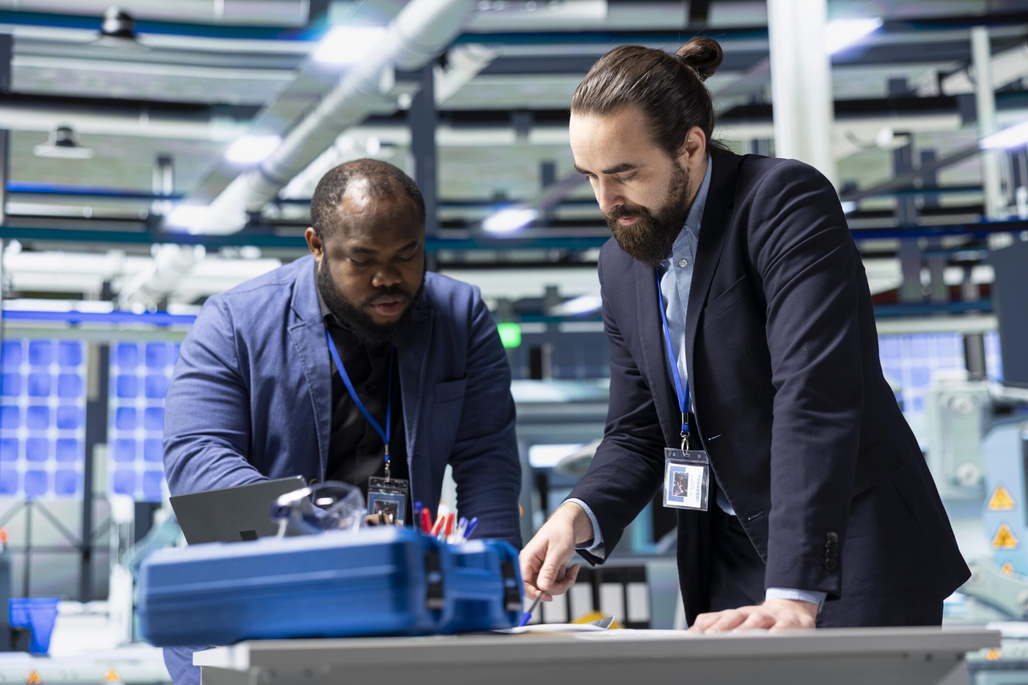 Two professionals in a modern lab bend over a workstation, examining tools and documents.